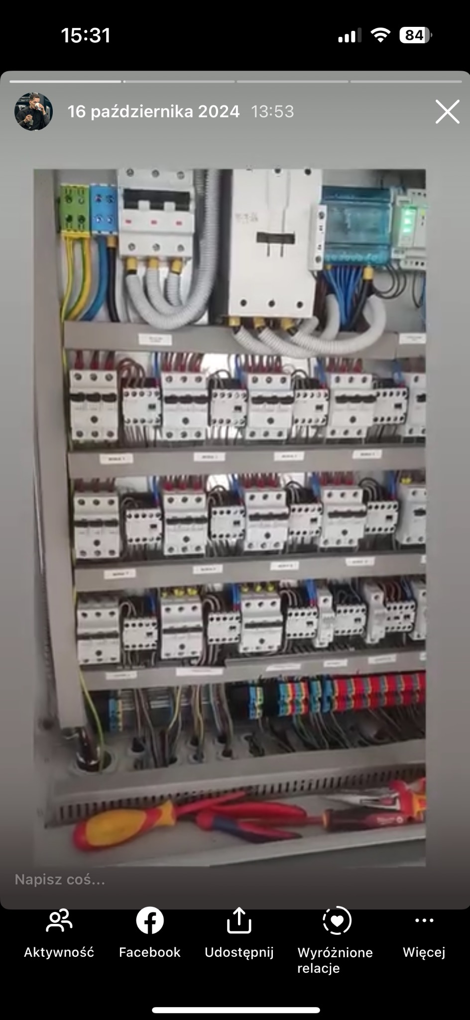 Otwarta szafa sterownicza z licznymi przekaźnikami, bezpiecznikami i okablowaniem, z żółto-czerwonym śrubokrętem i szczypcami leżącymi na dolnej półce.