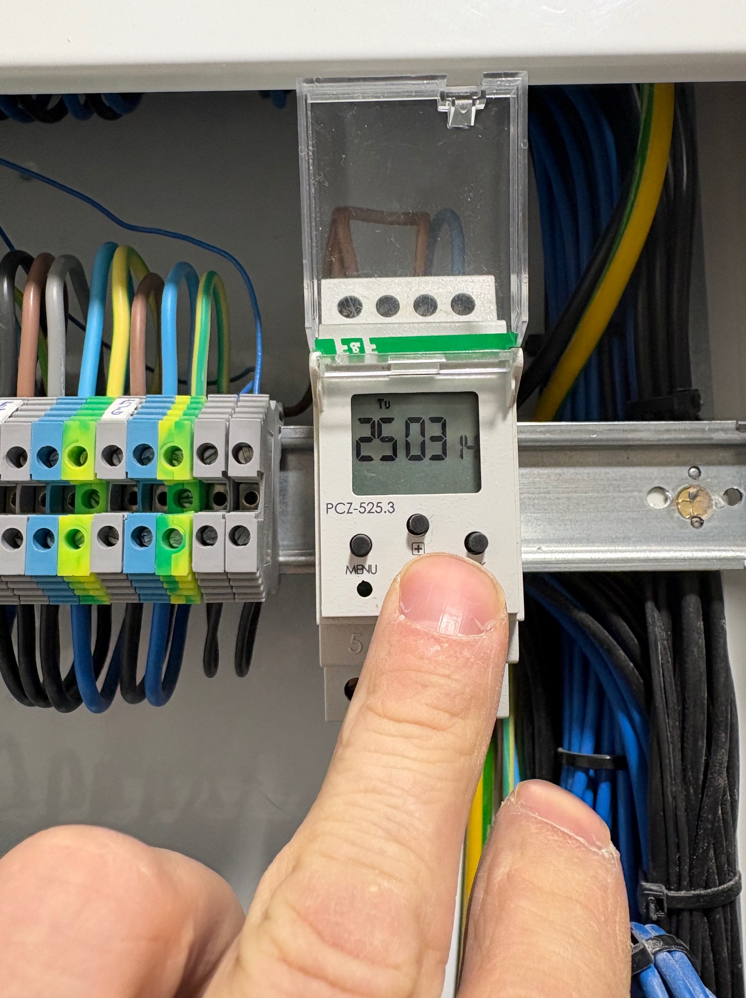 Ustawianie zegara sterującego w rozdzielnicy elektrycznej. Widoczne przewody, listwa zaciskowa i palec naciskający przycisk. Model PCZ-525.3.