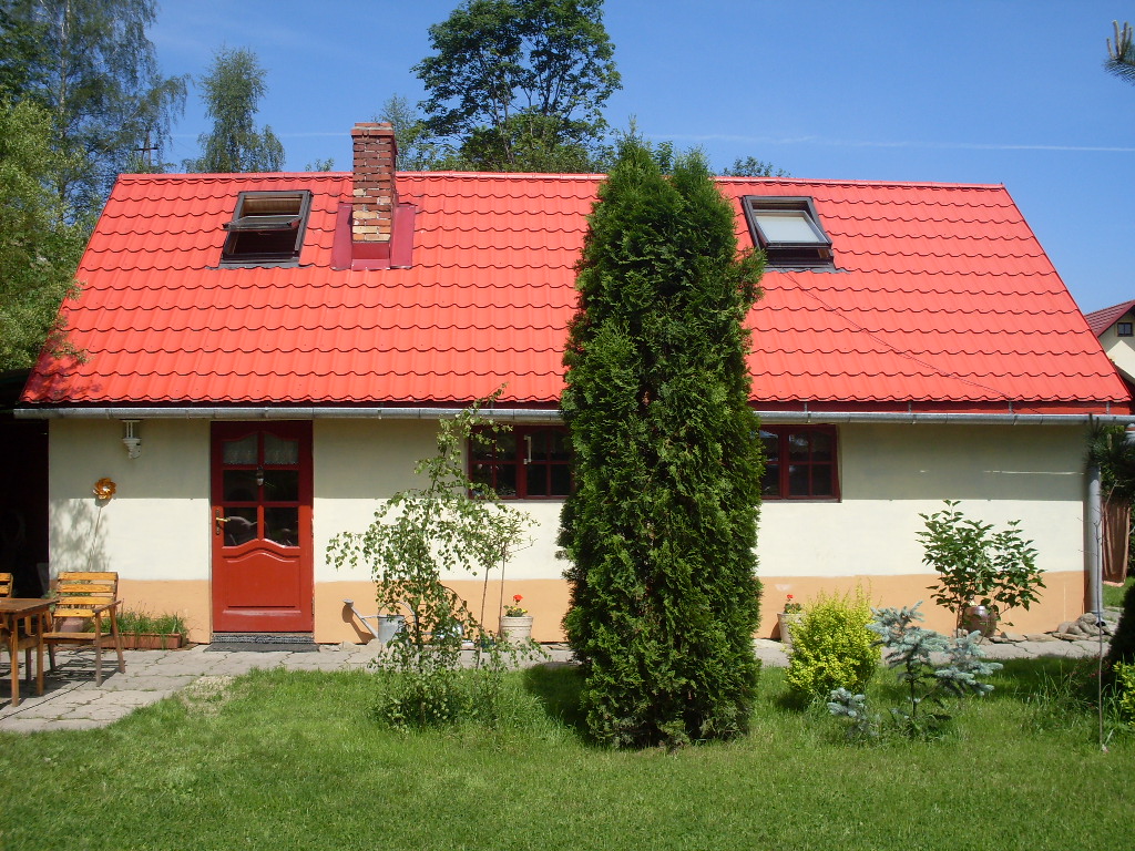 Dom w Suchej Beskidzkiej z czerwonym dachem, widok z ogrodu, z charakterystyczną wysoką tują na pierwszym planie.