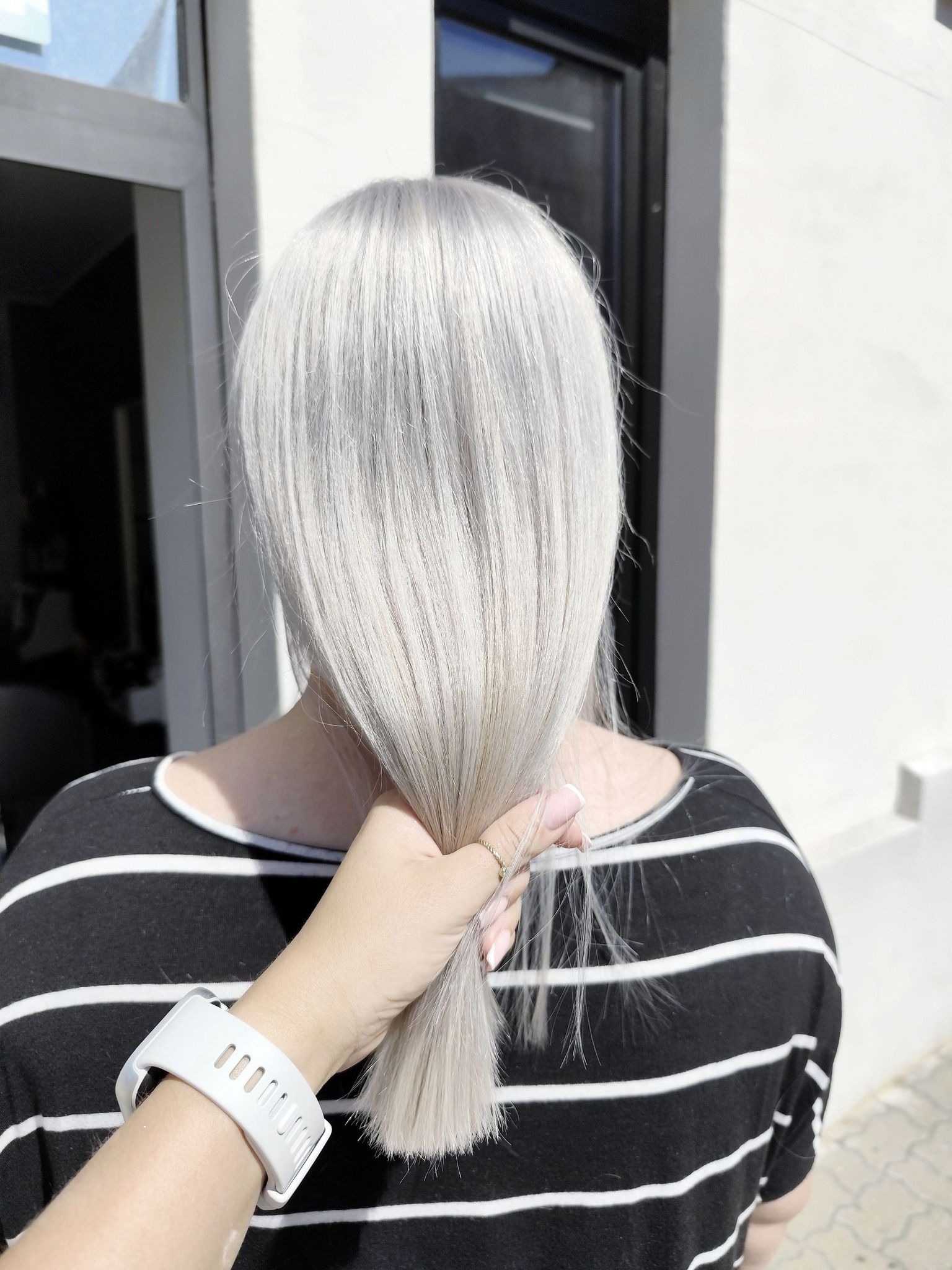 Tył głowy kobiety z długimi, platynowymi włosami trzymanymi w dłoni, ukazując efekt koloryzacji przy naturalnym świetle.