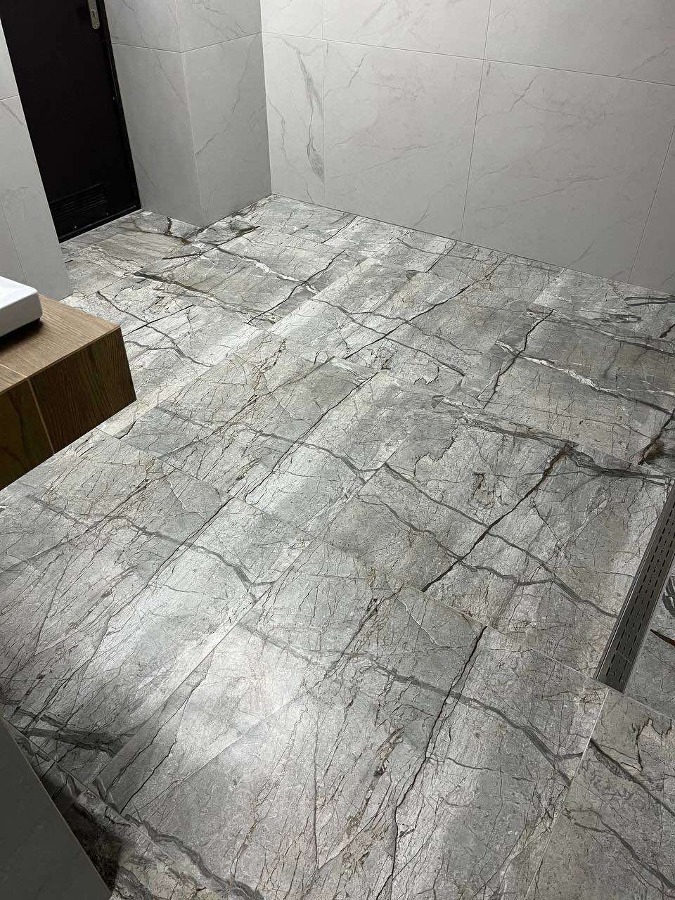 Wykończona łazienka z szarymi płytkami imitującymi marmur na podłodze i ścianach, widoczny odpływ liniowy pod prysznicem.