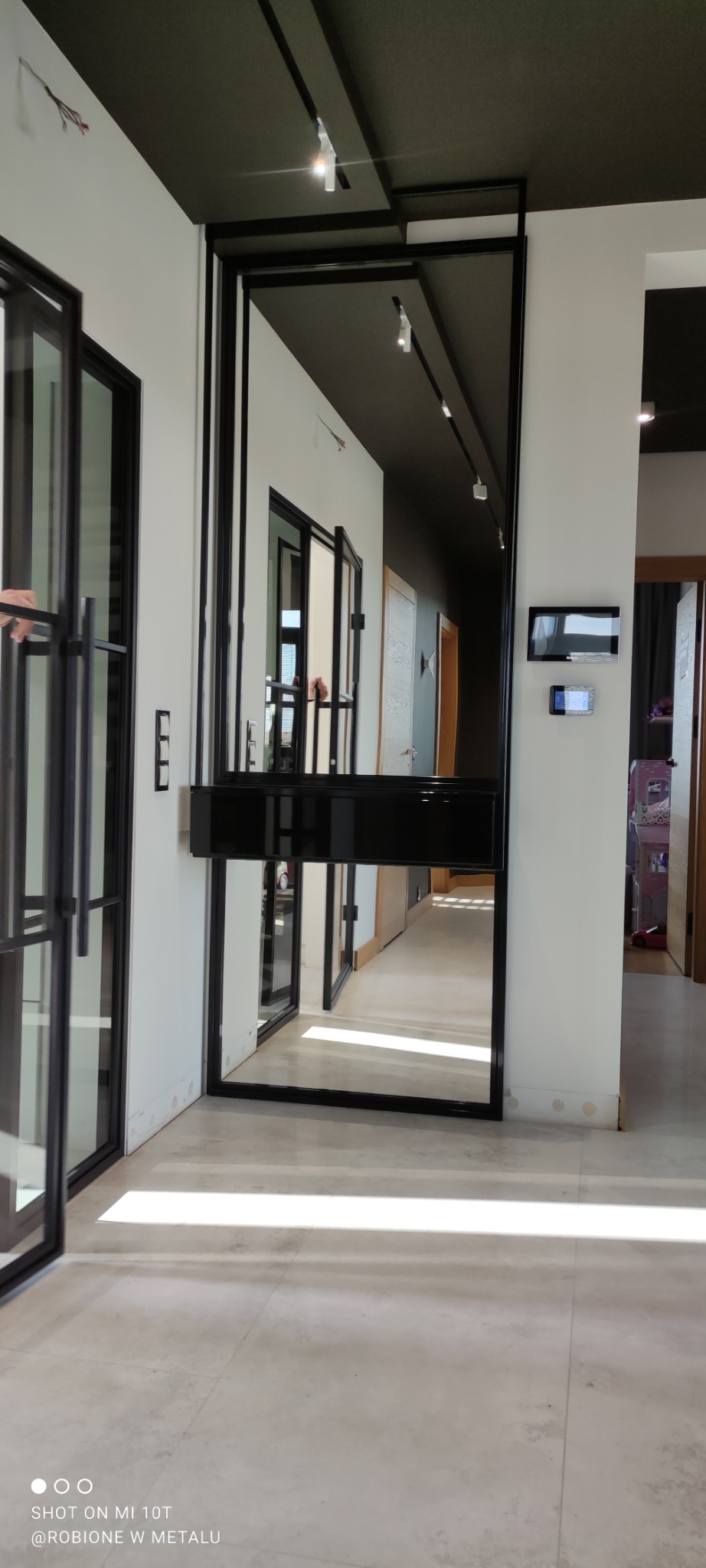 Nowoczesne drzwi szklane z czarną ramą w długim korytarzu, widok z boku, minimalistyczny design.