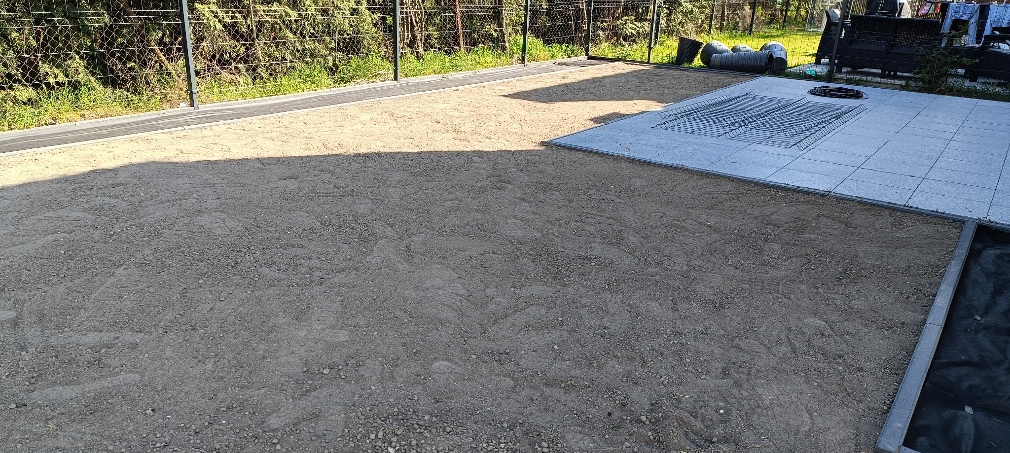 Przygotowanie terenu pod trawnik w Tarnowie Podgórnym: wyrównana powierzchnia z piasku, ułożone płyty betonowe i siatka zbrojeniowa. Widoczne obrzeża i agrowłóknina.