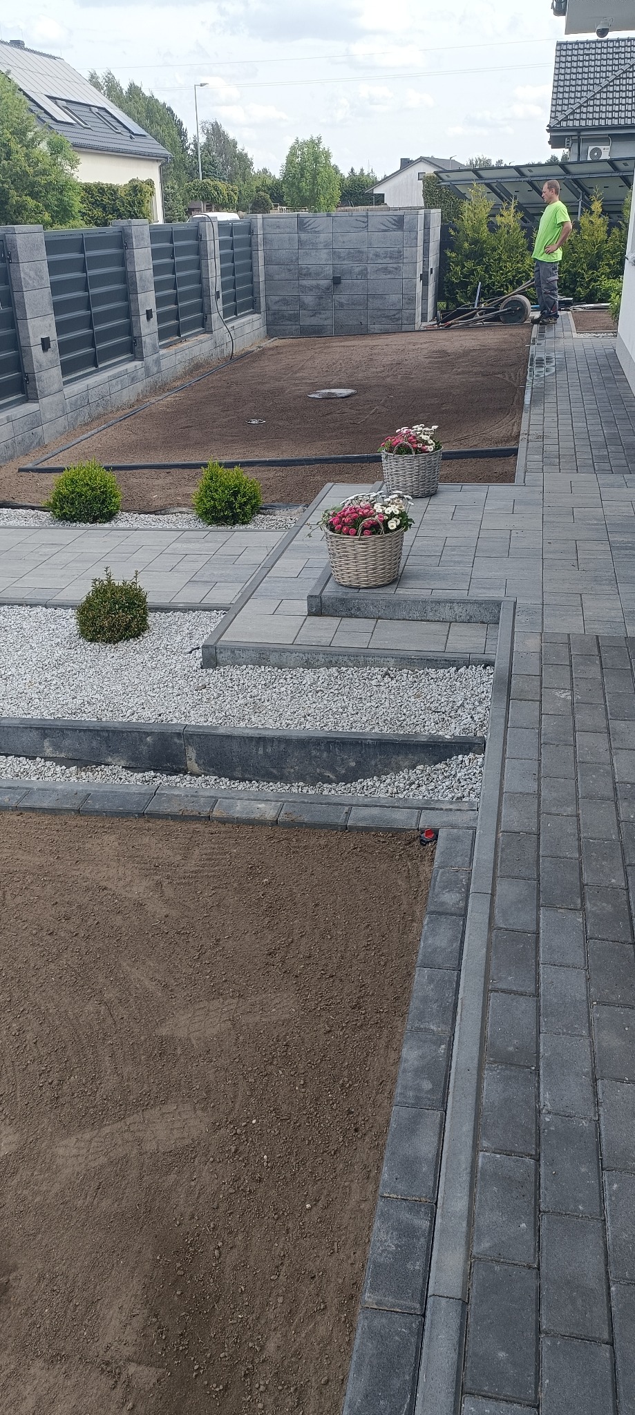 Przygotowany teren pod trawnik, obrzeża z kostki, dekoracyjny grys, kosze z kwiatami, krzewy i nowoczesne ogrodzenie panelowe. Prace ogrodnicze w toku.
