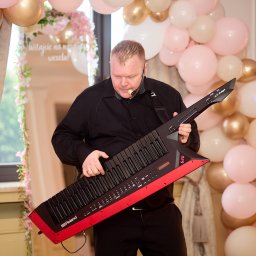 MARTEX MARCIN GAJEWSKI - Muzyk z keytar Roland AX-Edge 620 w Otwocku, ubrany na czarno, gra na tle dekoracji balonowych. Scena weselna, profesjonalne nagłośnienie.