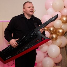 MARTEX MARCIN GAJEWSKI - Muzyk z keytarem Roland AX-Edge na tle dekoracji z balonów w odcieniach różu i złota. Ujęcie z występu na imprezie.