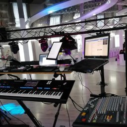 MARTEX MARCIN GAJEWSKI - Stanowisko DJ-a z klawiaturą, mikserem, laptopami i oświetleniem scenicznym, gotowe do występu na tle sali bankietowej z dekoracjami.