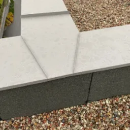 Szary dach pokryty kroplami deszczu, widoczne obróbki blacharskie i kamyczki na dachu, w tle budynek mieszkalny z zielenią.