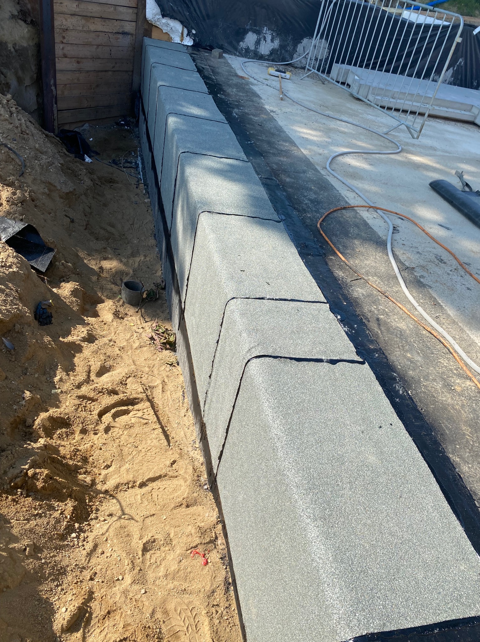 Świeżo ułożony szary obrzeże z kostki brukowej na podsypce piaskowej, widoczne narzędzia i zabezpieczenia na dalszym planie.