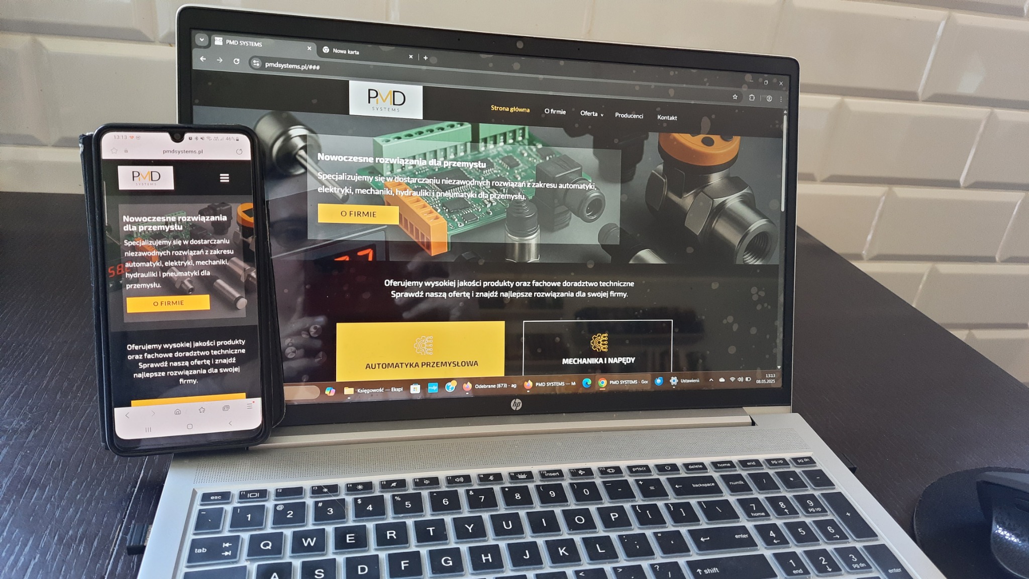 Laptop i smartfon wyświetlają stronę internetową pmdsystems.pl z elementami automatyki przemysłowej. Widoczny interfejs strony, menu i treść oferty firmy.