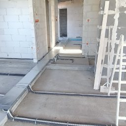 Michał Wysiecki - Usługi Elektryczne Smart Home - Wnętrze w trakcie prac elektrycznych: kable w peszlach i korytach ułożone na podłodze, widoczne puszki instalacyjne w ścianach z betonu komórkowego.
