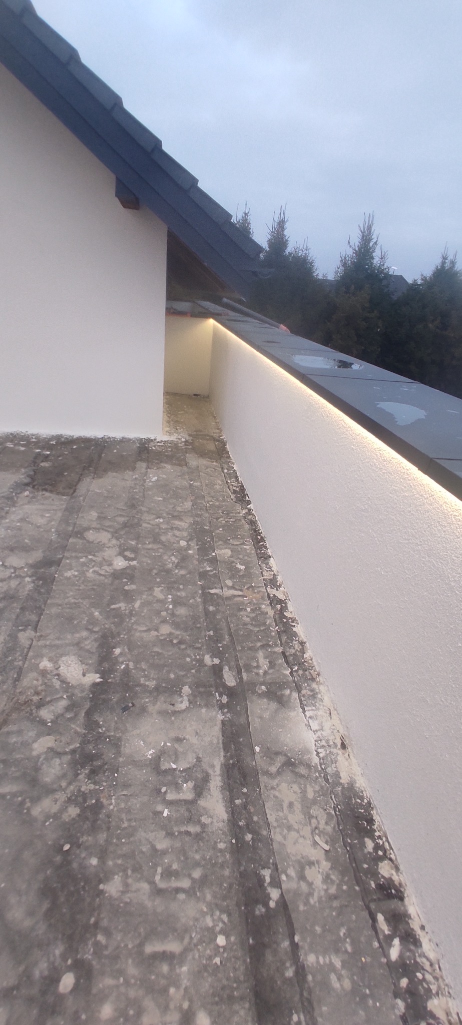 Nowoczesne oświetlenie LED na krawędzi dachu domu, z widoczną strukturą pokrycia dachowego i fragmentem elewacji. Minimalistyczny design i subtelne światło.