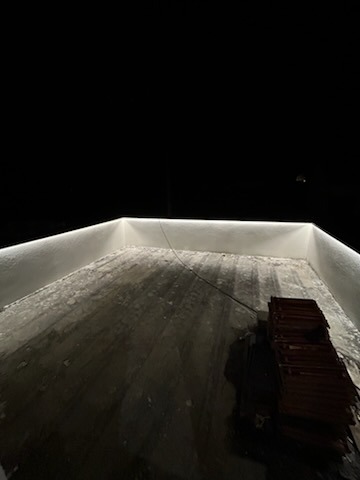 Białe, ledowe oświetlenie zamontowane wzdłuż krawędzi ścian, na tle ciemnej podłogi i czarnego nieba. Widoczne przewody i stos płytek.