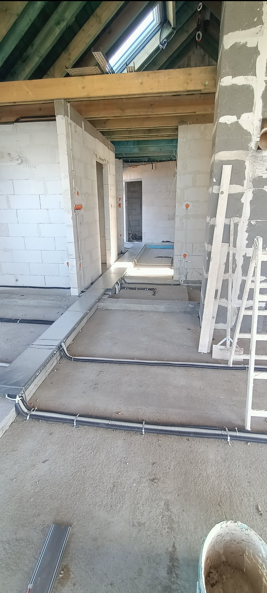 Wnętrze w trakcie prac elektrycznych: kable w peszlach i korytach ułożone na podłodze, widoczne puszki instalacyjne w ścianach z betonu komórkowego.