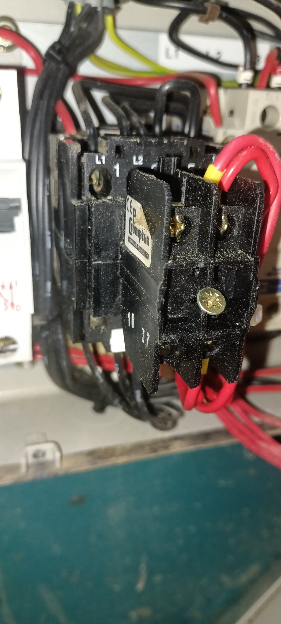 Czarny stycznik elektryczny marki Crompton z widocznymi śrubami, przewodami w kolorach czerwonym, żółtym i czarnym, zamontowany w skrzynce elektrycznej.