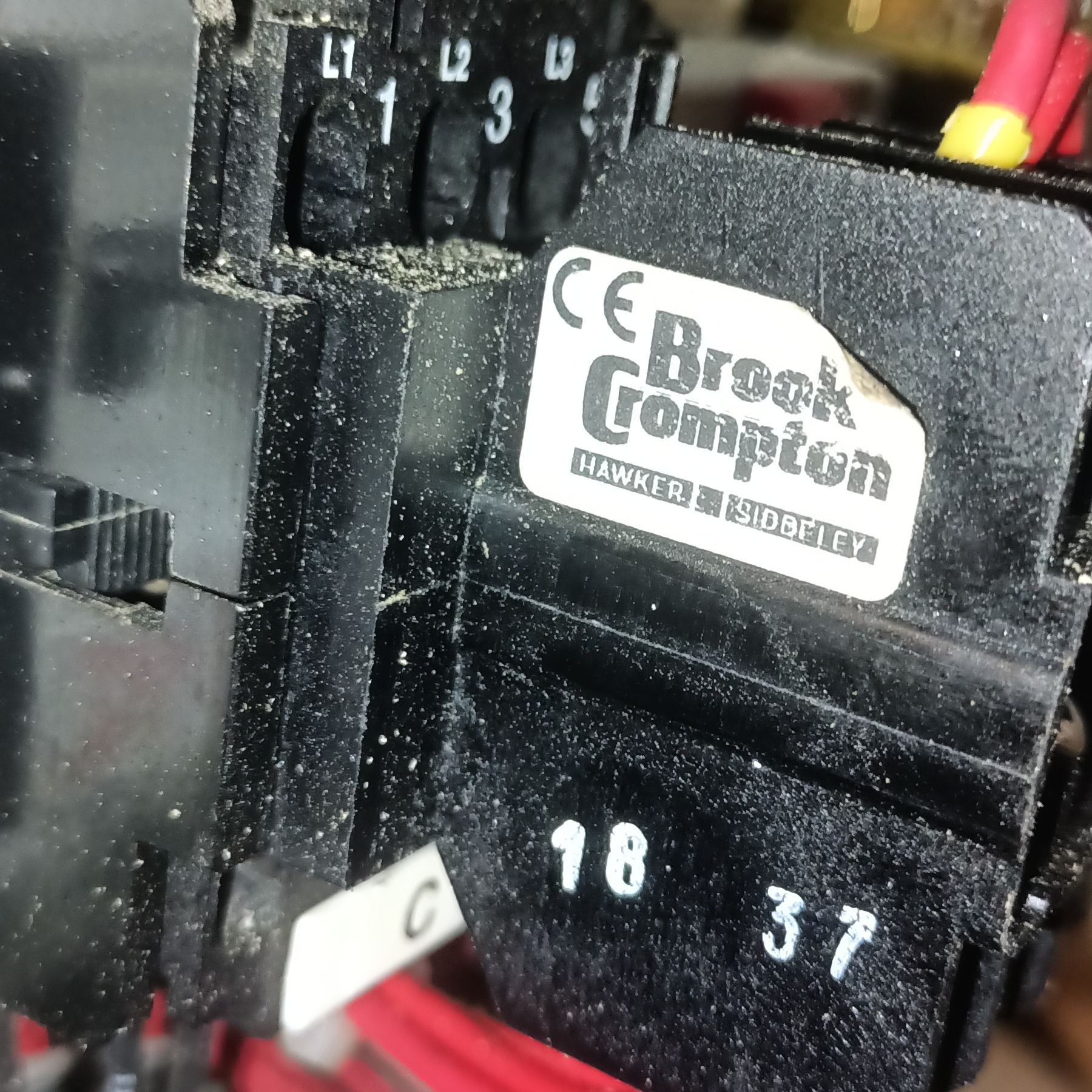 Czarny stycznik elektryczny Brook Crompton z oznaczeniami L1, L2, L3, 18 i 37, widoczne przewody w tle. Sprzęt elektryczny w zbliżeniu.