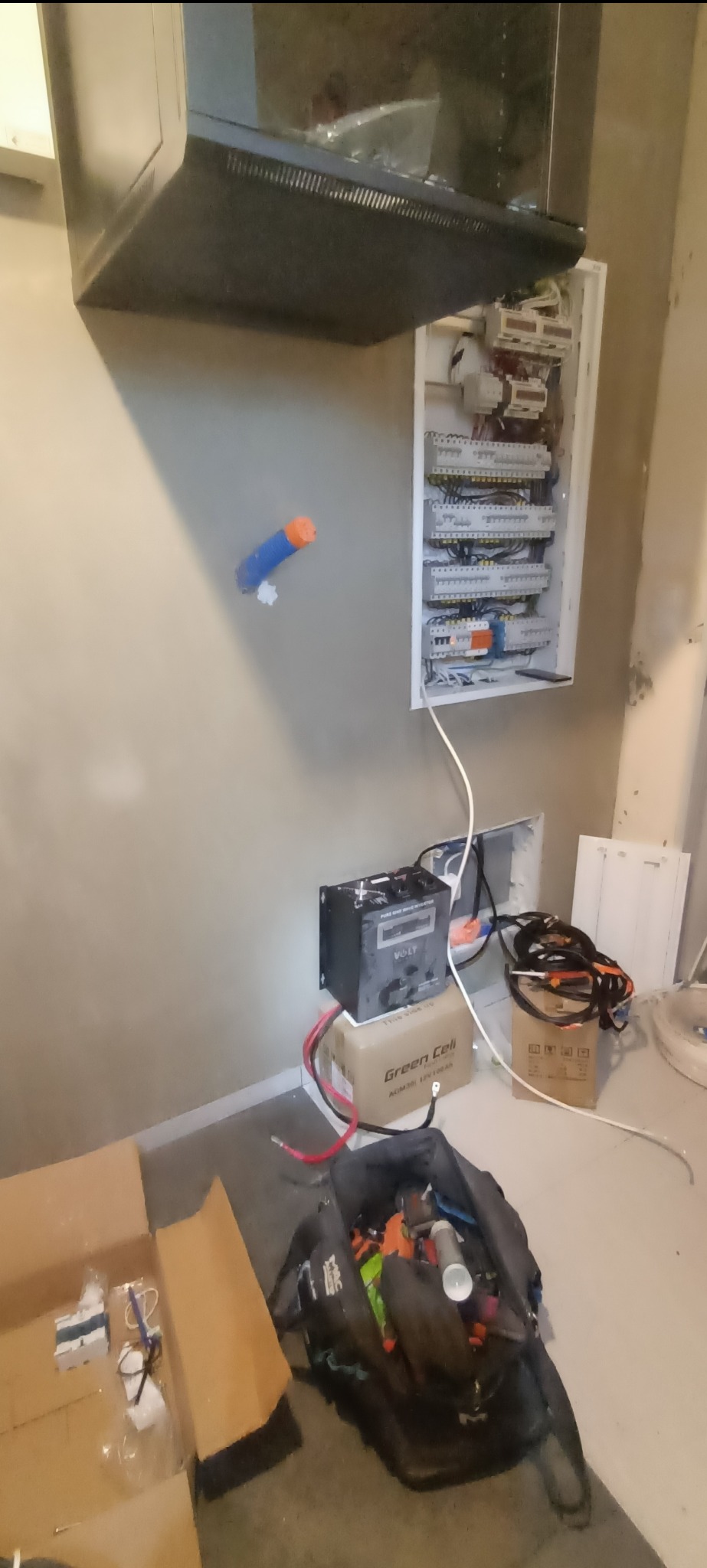 Rozdzielnica elektryczna z podłączonym zasilaniem awaryjnym, widoczne kable i skrzynka z narzędziami, ściana w trakcie wykończenia.