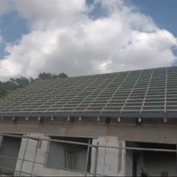 Konstrukcja dachu z łatami drewnianymi na czarnej membranie, widok z dołu na tle błękitnego nieba z chmurami, budynek w trakcie budowy z widocznym rusztowaniem.