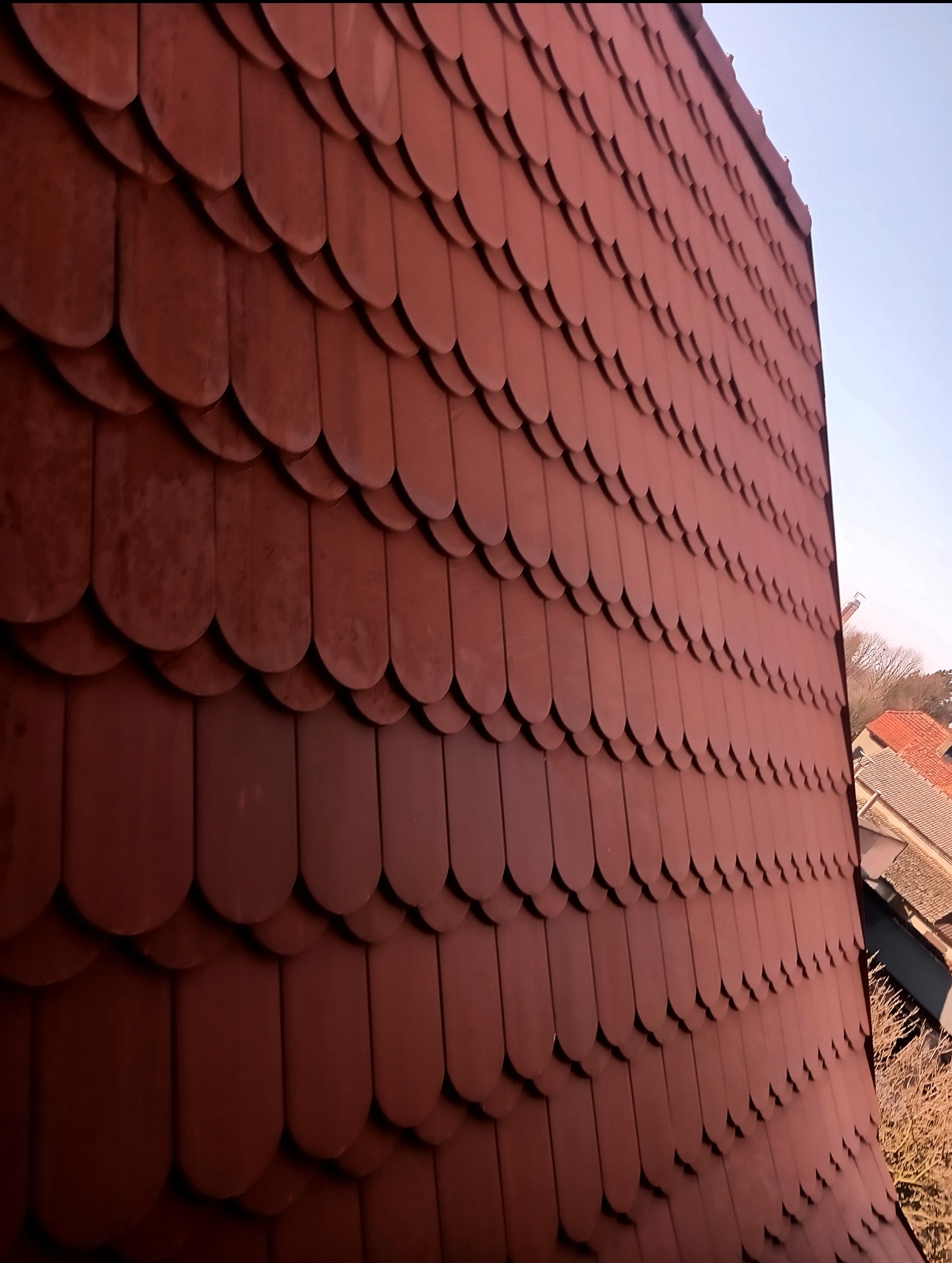 Czerwona dachówka karpiówka ułożona łuskowo na skośnym dachu, widok z dołu w słoneczny dzień.