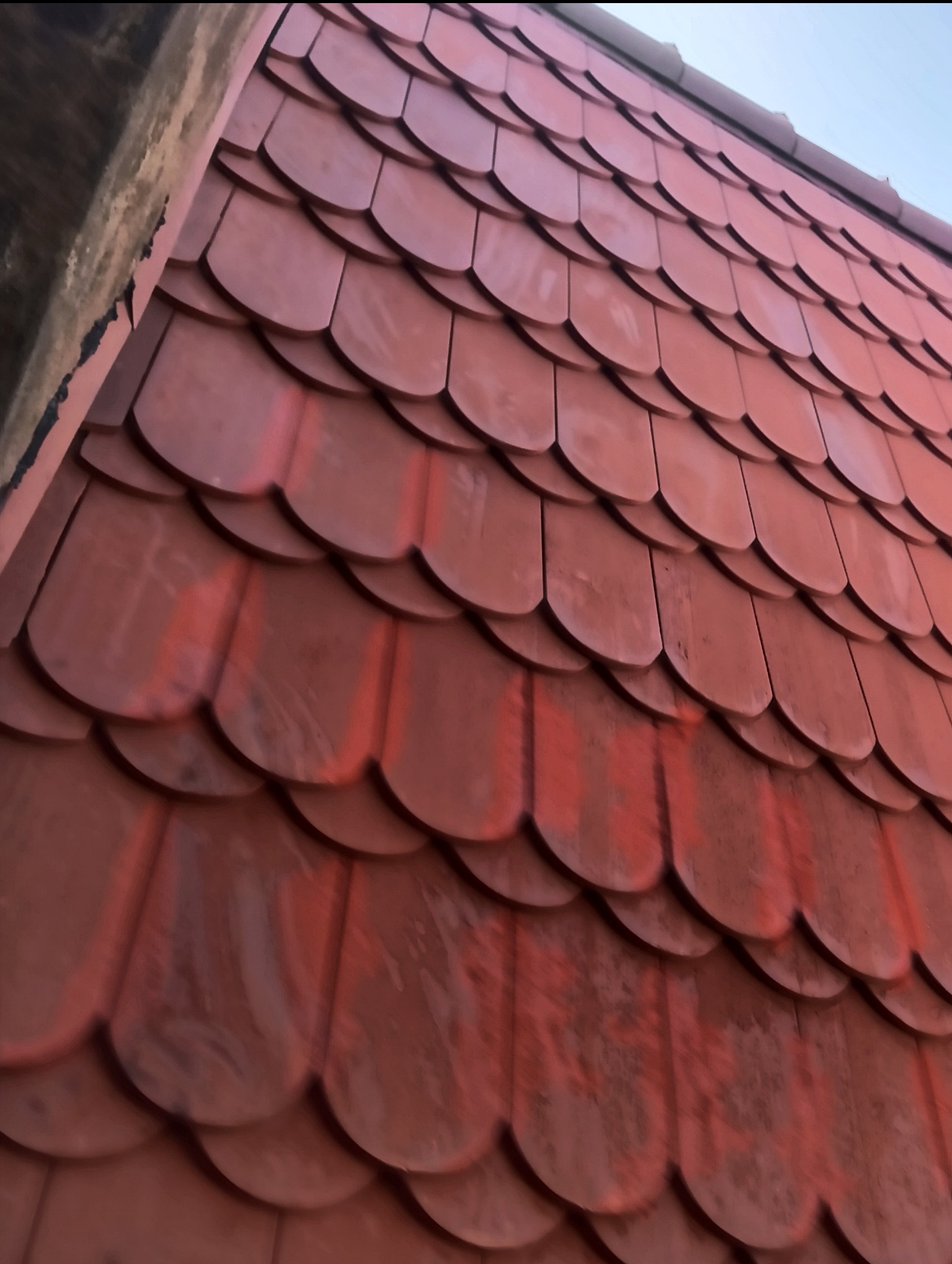 Czerwona dachówka karpiówka ułożona na dachu, widoczne zabrudzenia na powierzchni dachówek, fragment komina w lewym górnym rogu.