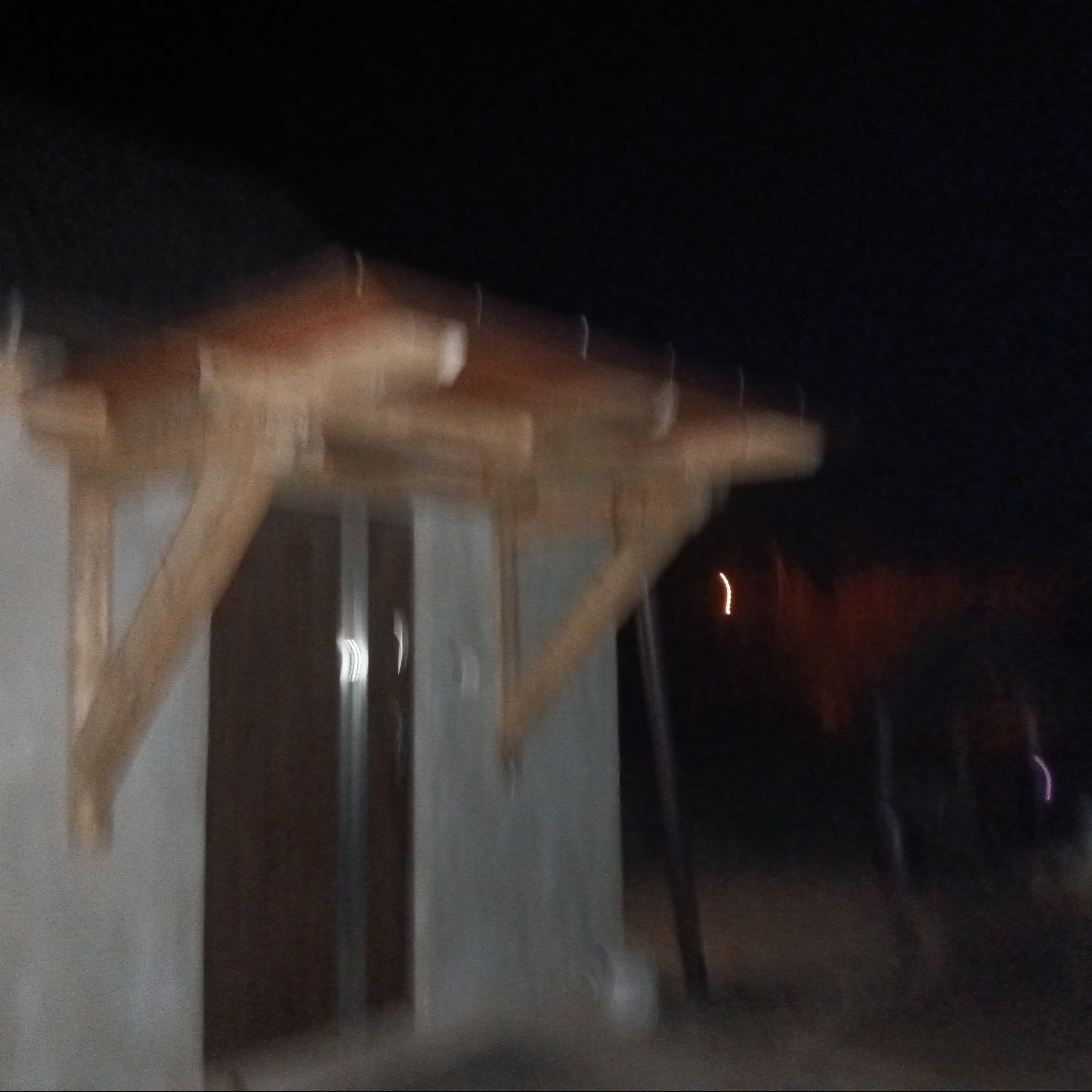 Niedokończona drewniana konstrukcja zadaszenia nad wejściem do budynku, widoczna w słabym oświetleniu nocnym.