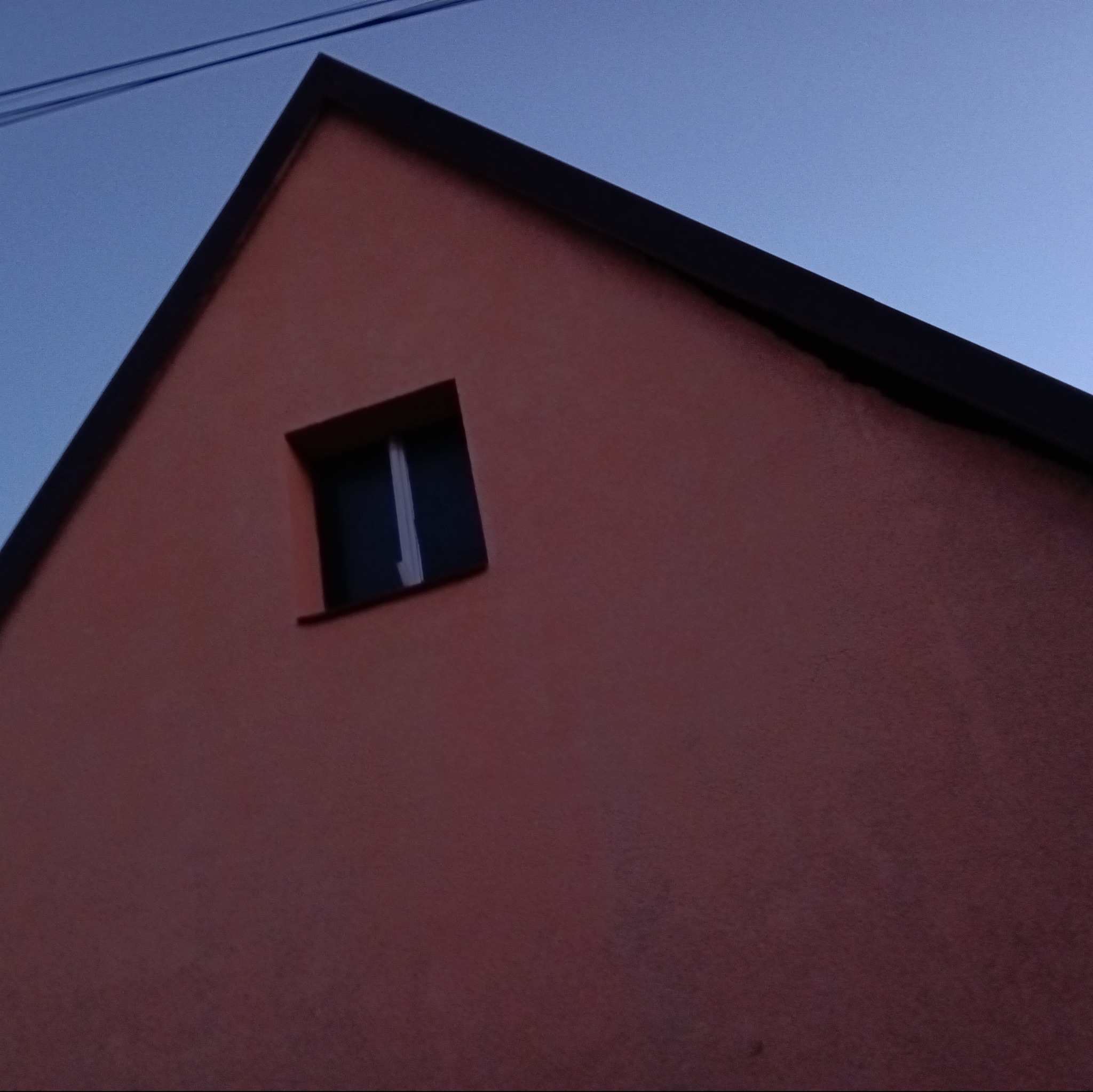 Fragment elewacji domu z dachem dwuspadowym i małym, kwadratowym oknem na poddaszu, sfotografowany pod kątem w pochmurny dzień.