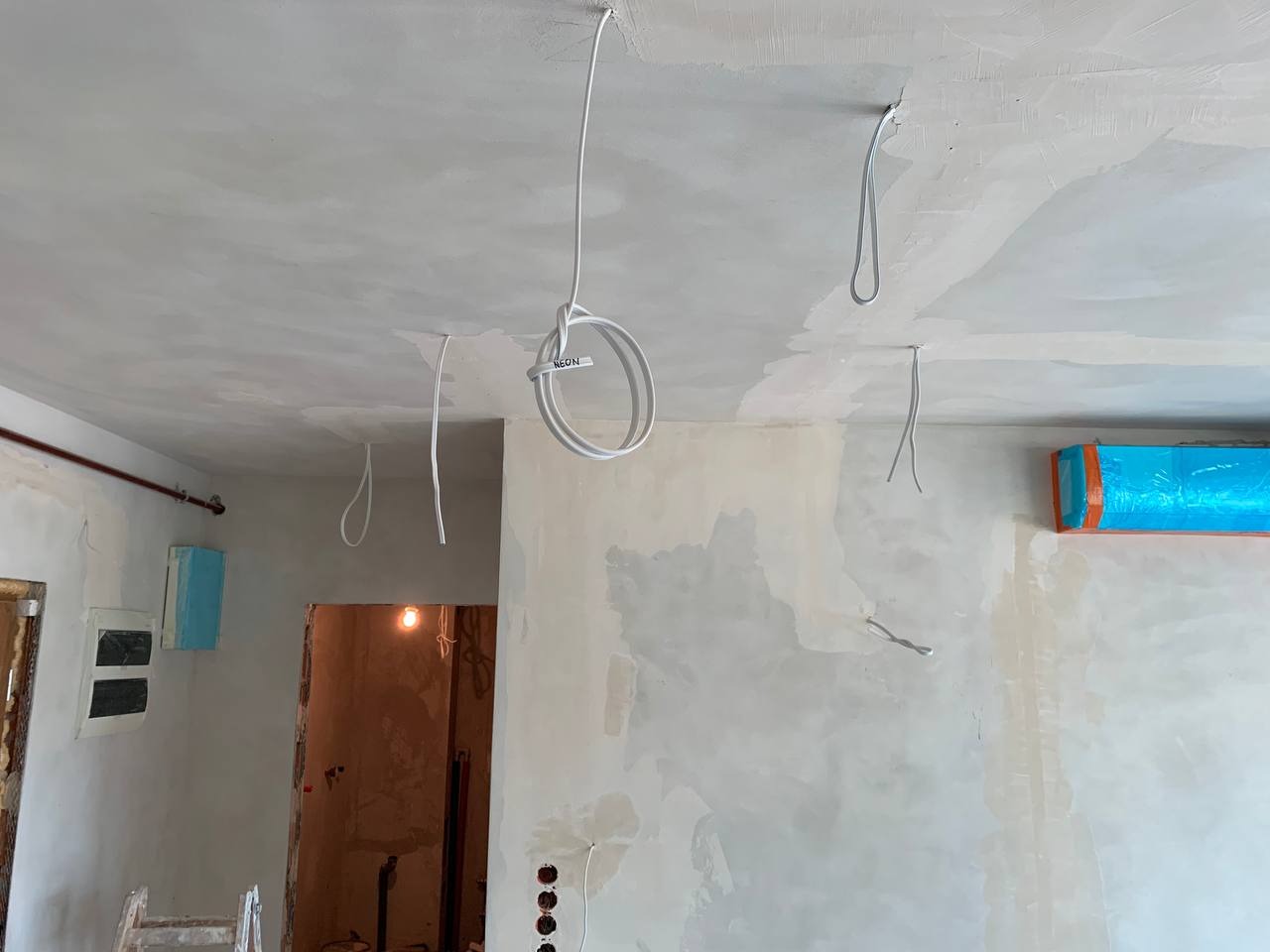 Wnętrze w trakcie remontu z widocznymi przewodami elektrycznymi wystającymi z sufitu i ścian, ściany przygotowane pod malowanie, widoczna instalacja elektryczna w puszce pod tynkiem...