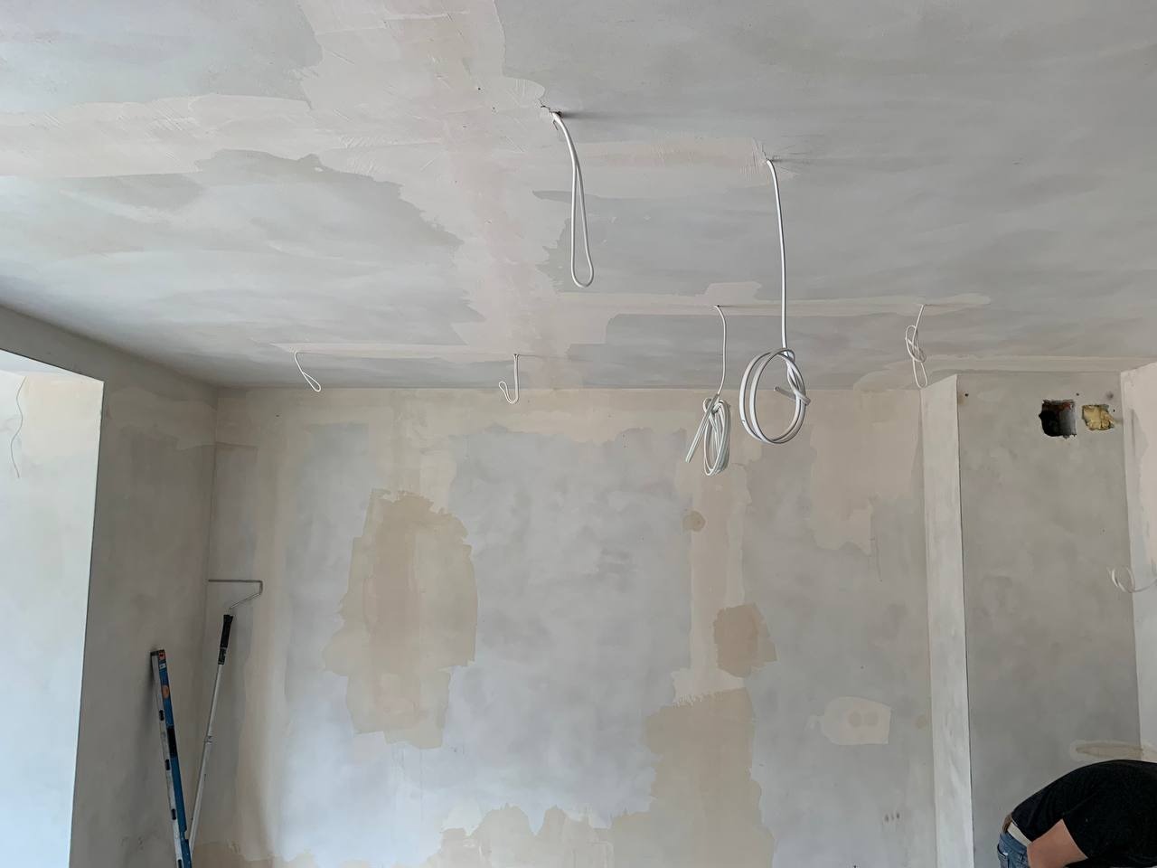 Wnętrze w trakcie remontu: świeżo zagruntowane ściany i sufit z wystającymi przewodami elektrycznymi, przygotowane do dalszych prac wykończeniowych.