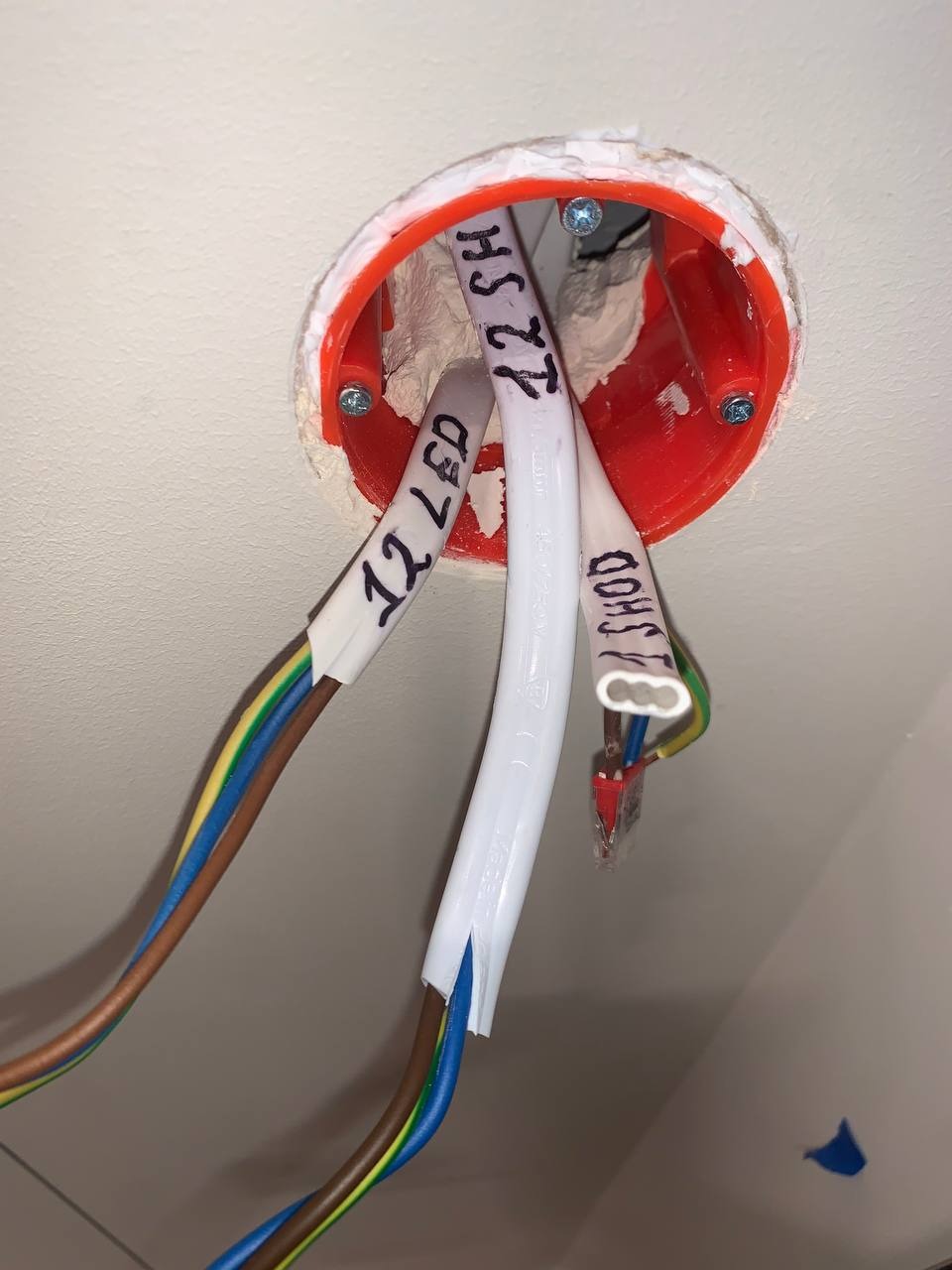 Otwór w suficie z widocznymi przewodami elektrycznymi oznaczonymi napisami '12 LED', '22 SH' i 'SHOD', wychodzącymi z czerwonej puszki instalacyjnej, zabezpieczonej białym uszczelniaczem.
