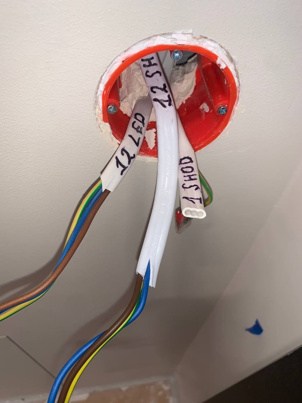 Otwór w suficie z widoczną pomarańczową puszką instalacyjną, z której wystają przewody elektryczne z oznaczeniami '12 LED', '1 SHOD' i '12 SH'.