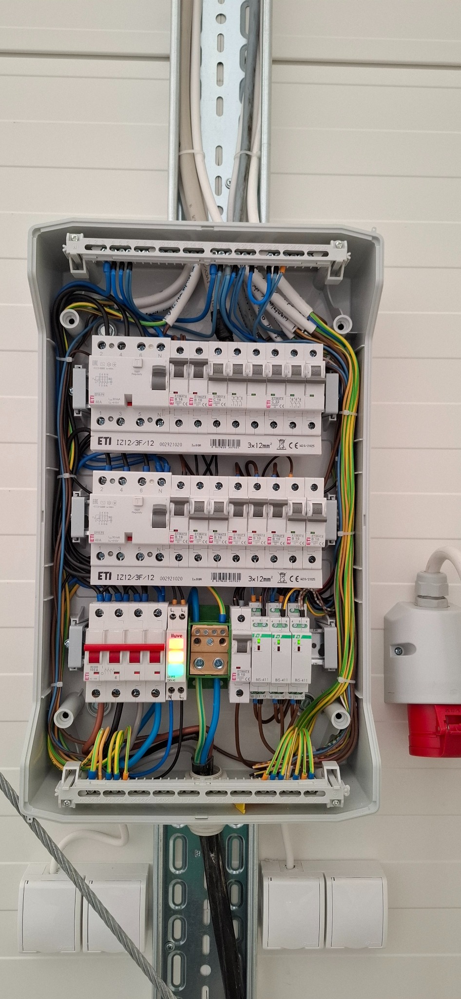 Rozdzielnica elektryczna z bezpiecznikami ETI, przewodami w kolorach niebieskim, żółto-zielonym i brązowym. Widoczne listwy zaciskowe i wyłączniki różnicowoprądowe.