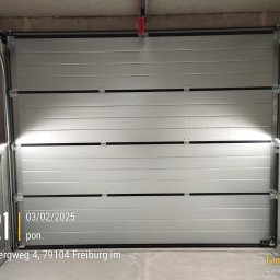 El Toro - Zamknięta, segmentowa, srebrna brama garażowa z widocznymi zawiasami i prowadnicami, sfotografowana od wewnątrz garażu. Na dole zdjęcia widoczny jest znak wodny z datą i godziną.