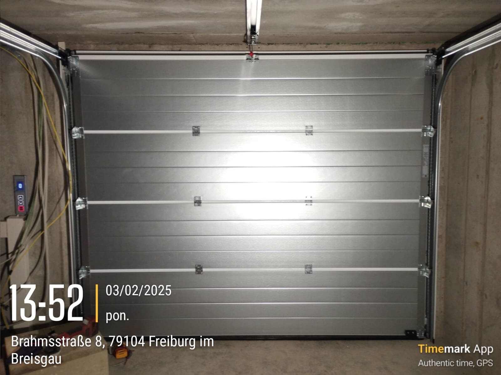 Zamknięta, segmentowa konstrukcja garażowa w kolorze srebrnym, widoczna z wnętrza garażu, z widocznymi elementami mocującymi i prowadnicami pod sufitem.