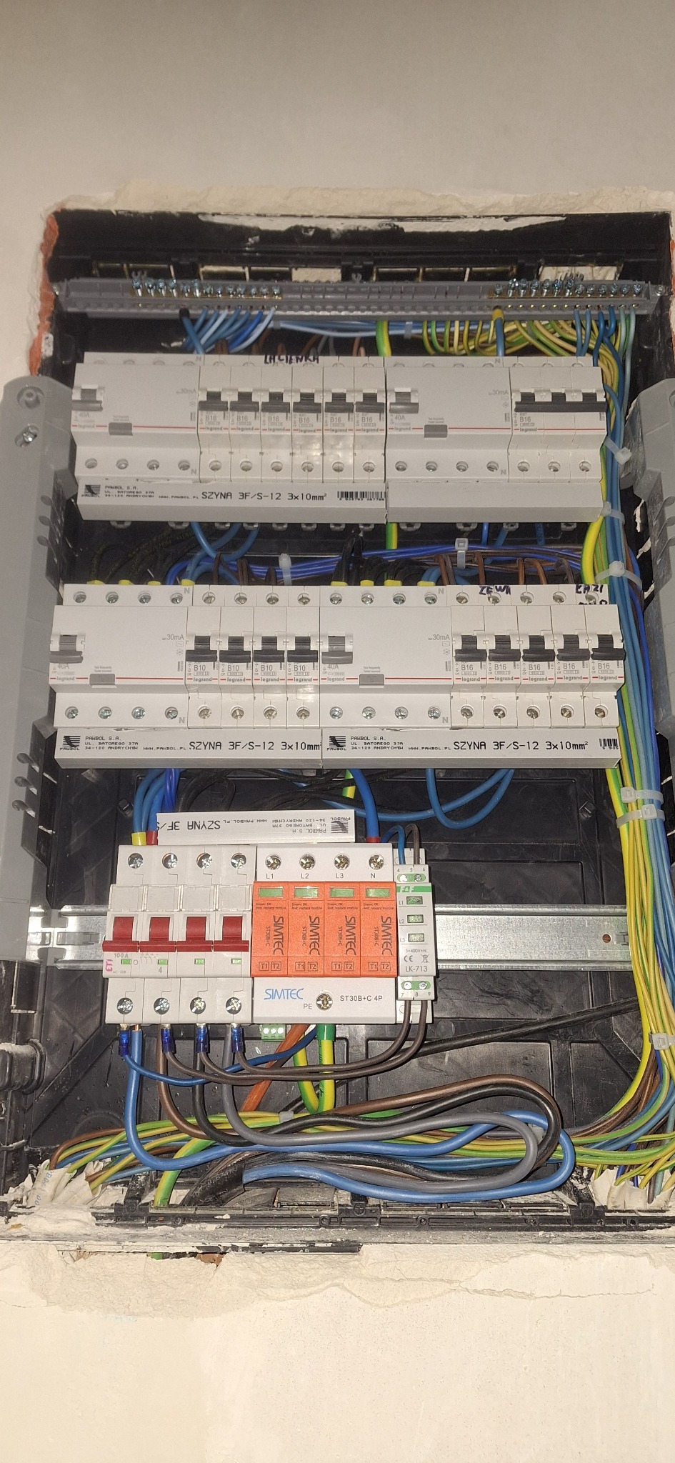 Rozdzielnia elektryczna z zainstalowanymi bezpiecznikami i przewodami. Widoczne elementy marki Legrand i Simtec.