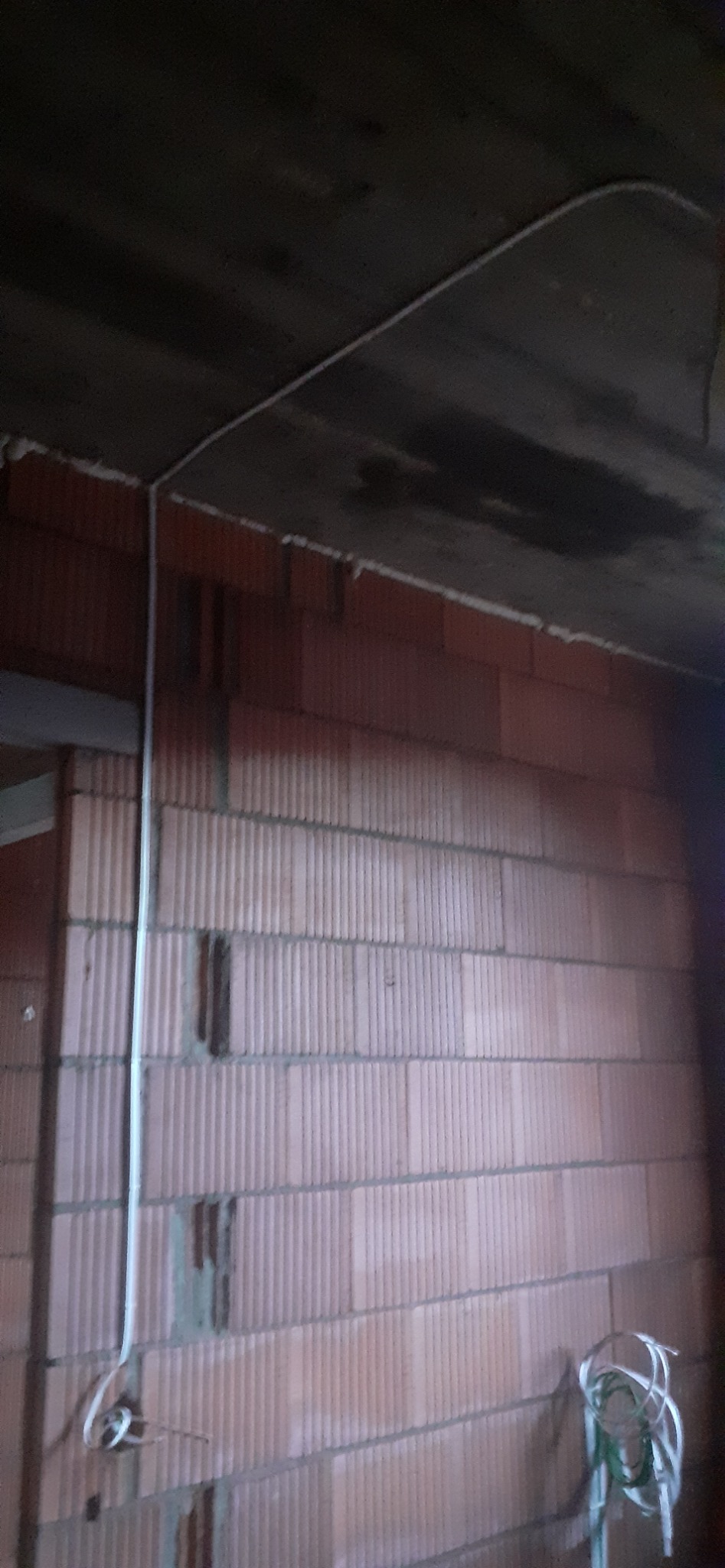 Wewnętrzna instalacja elektryczna w trakcie montażu: przewody poprowadzone po ceglanej ścianie, widoczne mocowania do sufitu. Etap prac przed tynkowaniem.