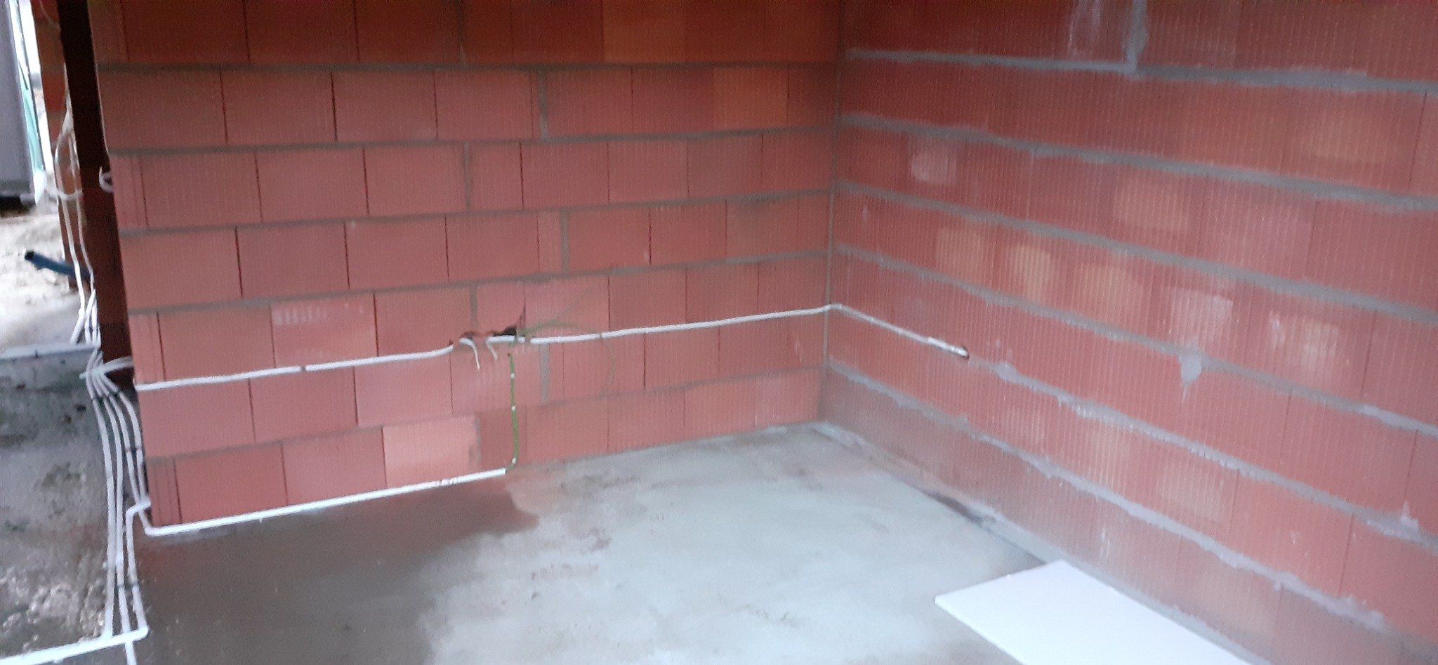 Surowe wnętrze z czerwonej cegły z widoczną białą instalacją elektryczną, kable prowadzone wzdłuż ścian. W tle widoczne inne pomieszczenia.