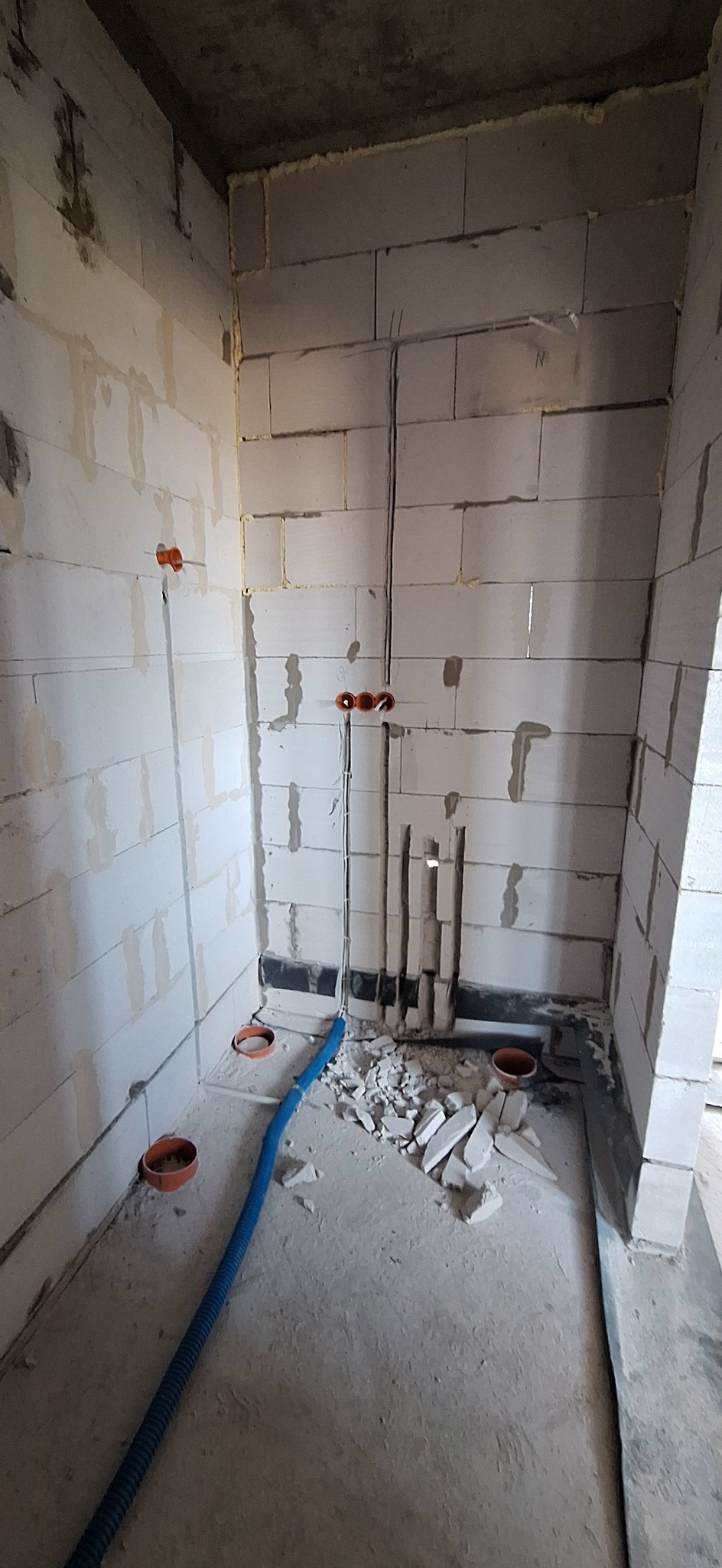 Surowy stan: Instalacja elektryczna w bruzdach ściany z betonu komórkowego. Widoczne kable, peszle i puszki instalacyjne. Podłoże z gruzem i niebieskim peszlem.