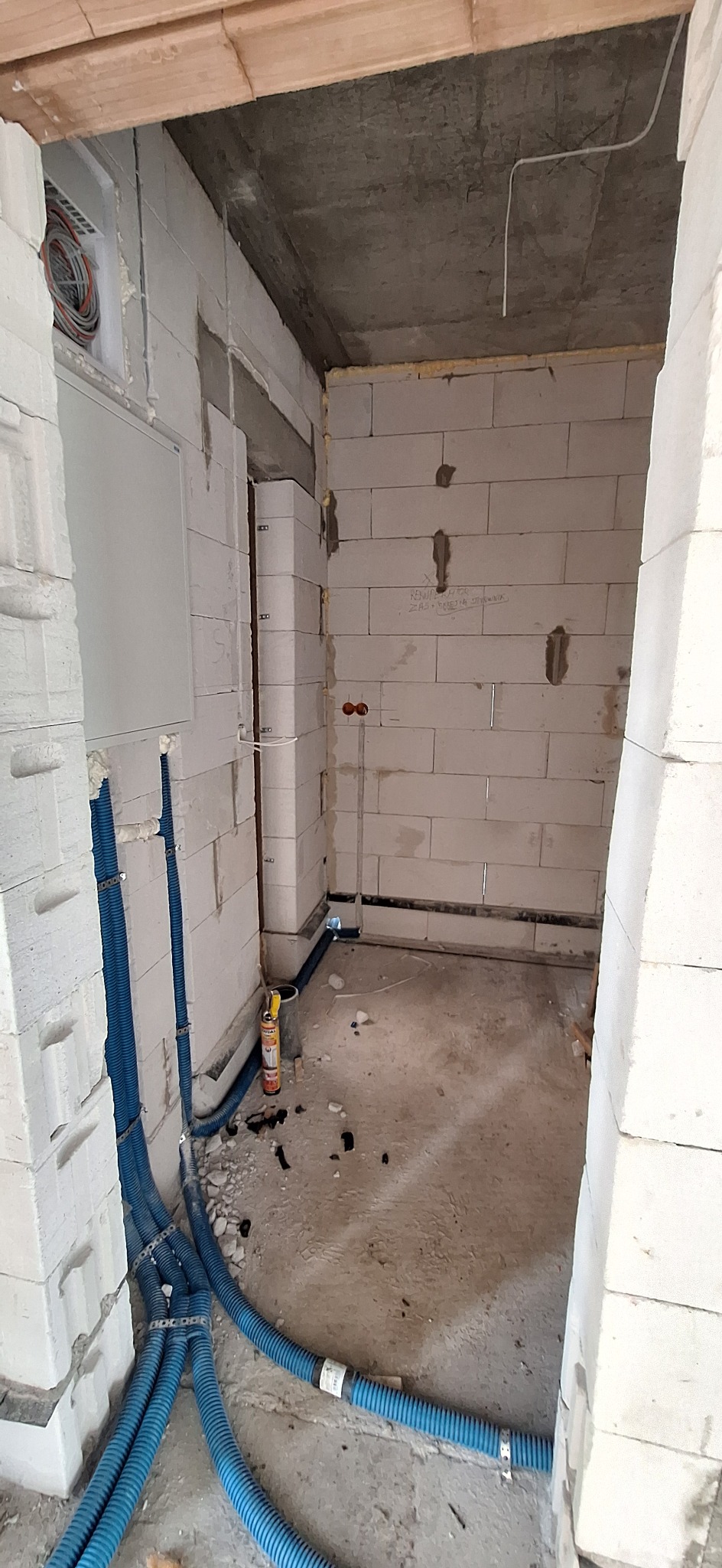 Surowy stan: Nieotynkowane ściany z betonu komórkowego, niebieskie rury instalacyjne i puszka elektryczna wewnątrz budynku w trakcie budowy.