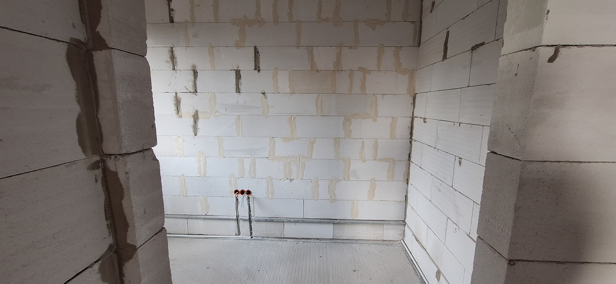 Wnętrze w trakcie budowy z widocznymi przewodami elektrycznymi w ścianie z białych bloczków. Instalacja w peszlu, puszki instalacyjne. Surowy stan.