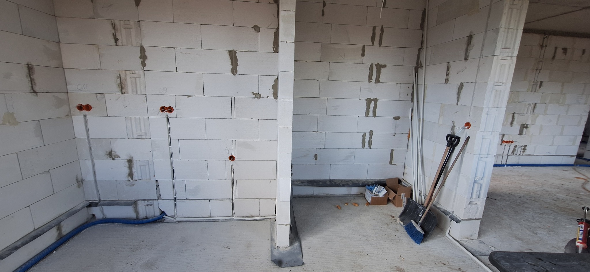 Surowy stan: instalacja elektryczna w ścianach z betonu komórkowego, widoczne peszle i puszki. Nieotynkowane ściany, podłoga wylewka, narzędzia w tle.