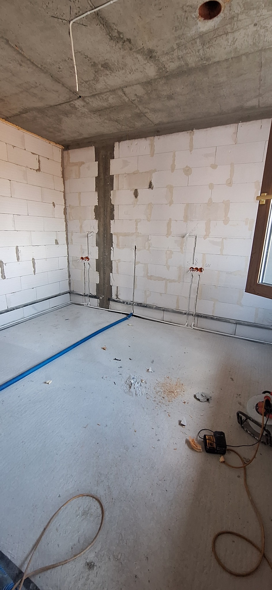 Surowy stan instalacji elektrycznej w Przygłowie: widoczne przewody w ścianach z betonu komórkowego, rury na podłodze i otwór w suficie. Etap prac wykończeniowych.