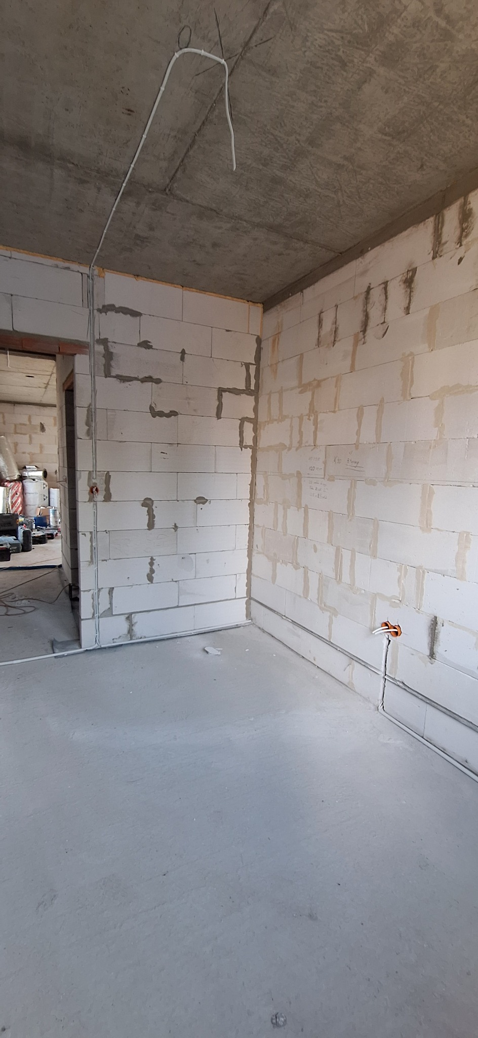 Surowy stan: wnętrze w trakcie prac instalacyjnych. Widoczne przewody elektryczne poprowadzone po ścianach z betonu komórkowego i pod sufitem. Gniazdka elektryczne w ścianach.