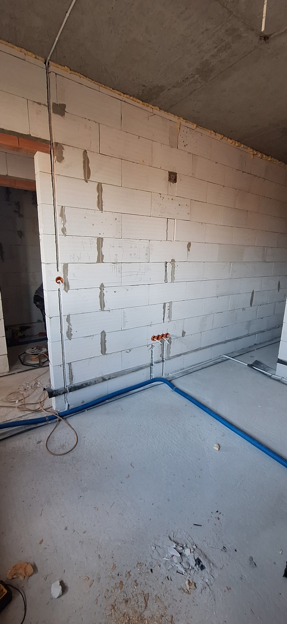 Wnętrze w trakcie prac: ściany z betonu komórkowego z bruzdami, w których poprowadzone są rury instalacji elektrycznej. Na ścianie widoczne schematy instalacji.