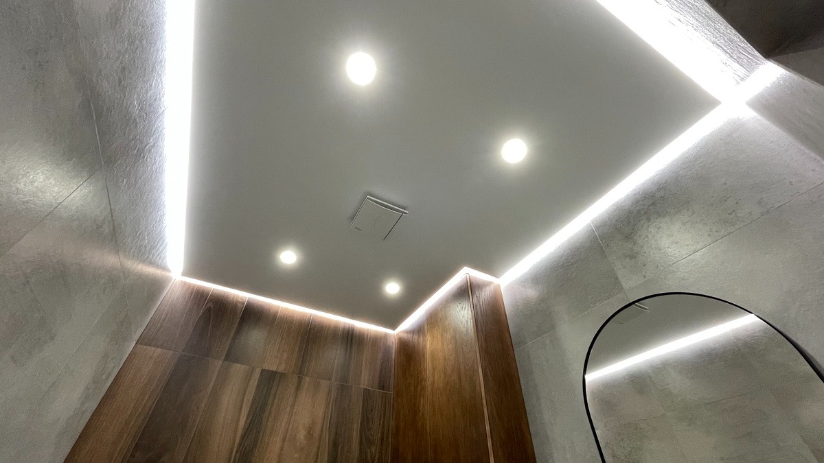 Nowoczesna łazienka z podświetlanym sufitem, punktowe oświetlenie i drewniane panele na ścianie.