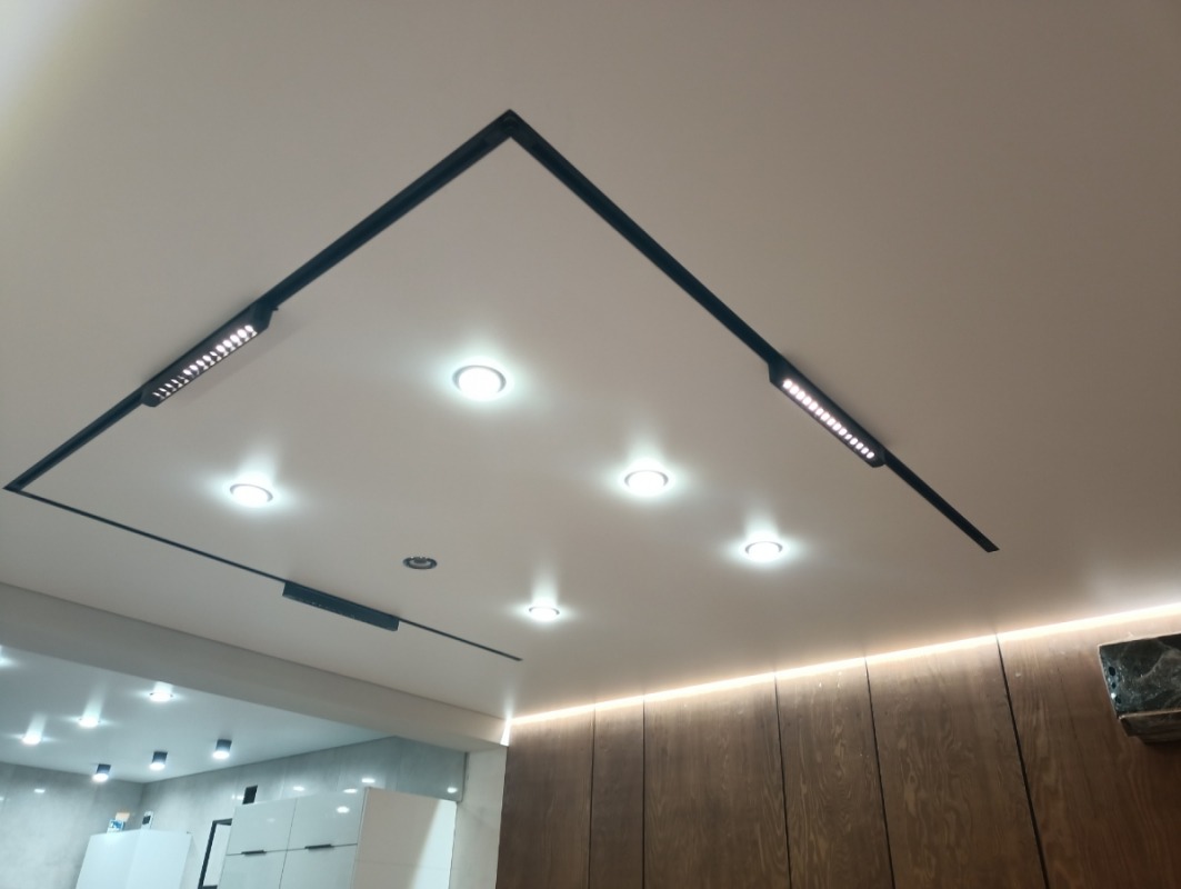 Biały sufit z wbudowanym oświetleniem LED w geometrycznym układzie, widoczne drewniane panele ścienne z podświetleniem.