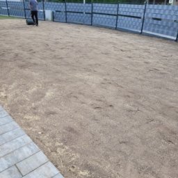 GARDEN USŁUGI OGRODNICZE GRZEGORZ TYMURA - Przygotowany teren pod trawnik z widocznym wałem i fragmentem kostki brukowej. W tle szary płot panelowy i zabudowa jednorodzinna.