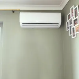 Biała jednostka klimatyzacji na ścianie w pokoju z zielonymi ścianami i ramkami ze zdjęciami.