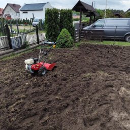 GreeenGarden Mateusz Kwidzinski - Czerwony glebogryzarek spalinowy na nierównej, przekopanej ziemi pod przyszły trawnik. W tle domy i szara furgonetka.