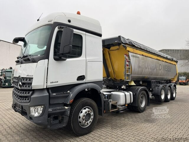 Ciężarówka Mercedes-Benz Actros 1843 z żółtą naczepą wywrotką, częściowo przykrytą plandeką, zaparkowana na brukowanej powierzchni, widok z boku na pochmurnym tle.