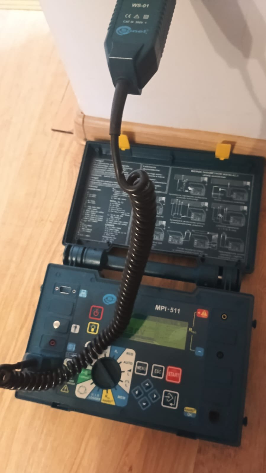 Miernik instalacji elektrycznych MPI-511 w otwartej obudowie, używany podczas pomiarów w Jakimowicach. Widoczny przewód pomiarowy i panel sterowania urządzenia.